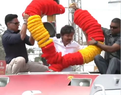 தாராபுரம் செல்லும் வழியில் தொண்டர் வழங்கிய பிரம்மாண்ட மாலை – அணிந்துகொண்டு எட்டிப்பார்த்து காட்டிய விஜய்!